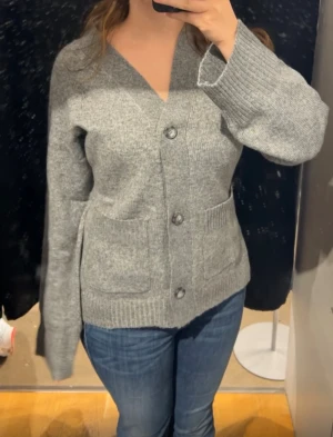 Lager 157 cardigan ”Sabrina”  - Mysig grå kofta med v-ringad hals och stora framfickor från lager157. Tröjan har långa ärmar och stängs med tre knappar framtill. Ribbstickade muddar vid ärmslut och nederkant ger en skön och avslappnad look. Perfekt att slänga på sig när det är lite kyligt.