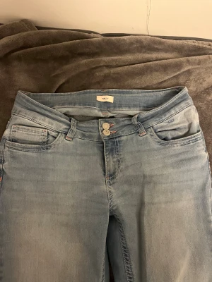 Bootcut jeans i ljusblå färg från Nelly - Snygga ljusblå bootcut jeans från Nelly med klassisk femficksdesign och dubbla knappar i midjan. Baktill har de coola broderade detaljer på fickorna i rosa och vitt. Dessa är knappt andvända. Jag är 175cm och de är perfekt i längden 💞