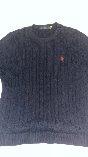 Mörkblå stickad tröja Polo Ralph Lauren - Säljer en mörkblå stickad tröja från Polo Ralph Lauren med klassiskt kabelstickat mönster och röd broderad logga på bröstet. Rund halsringning och ribbade muddar vid ärmslut och nederkant. Perfekt för dig som gillar stilrena och tidlösa plagg. Den kan passa folk i M också. Pris och byte kan diskuteras