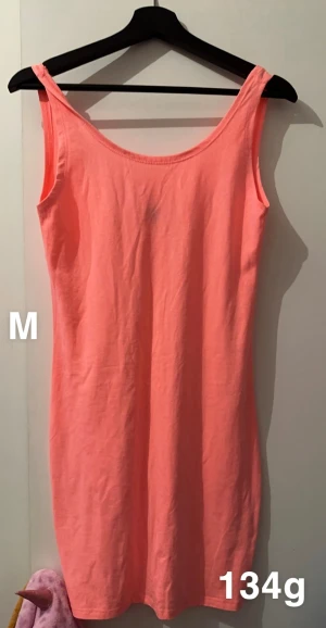 Korallrosa ärmlös klänning  - Snygg korallrosa klänning i mjukt material med enkel, rak passform och breda axelband. Perfekt för varma dagar och enkel att styla med accessoarer. Klänningen är ärmlös och har en klassisk rund halsringning.🌸 Fint skick. Lägre rygg. Storlek M