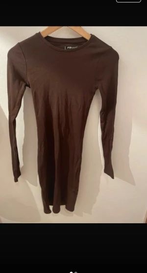 Brun långärmad klänning  - En enkel och stilren brun långärmad klänning . Klänningen har en kroppsnära passform och är tillverkad i mjuk bomull, perfekt för dig som gillar minimalistisk stil.