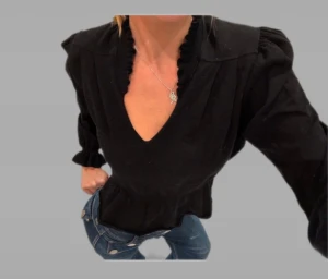 Svart blus med volang från ba&sh - Supersnygg svart blus från ba&sh med volangdetaljer vid halsringning och ärmslut. Blusen har v-ringad hals, puffade axlar och markerad midja med volang. Långärmad och tillverkad i mjuk bomull som känns skön mot huden. Perfekt för dig som gillar stilrena och coola plagg. Storlek S!!🩵Skickar snabbt