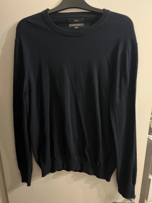 Mörkblå bomullströja från M&S XL - En stilren mörkblå tröja från M&S i ren bomull. Tröjan har rund hals, ribbade muddar och långärmad design. Perfekt för dig som gillar enkel och klassisk look med skön passform. Passar dig som vill ha en basic tröja i garderoben.