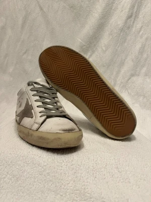 Golden Goose vita sneakers med grå stjärna - Snygga vita sneakers från Golden Goose. Skorna har blivit proffesionellt lagade på sidan utav skon som du kan se på näst sista bilden men är inget man tänker på🙌 annars ingen fara!👍passar mellan 40-41,5
