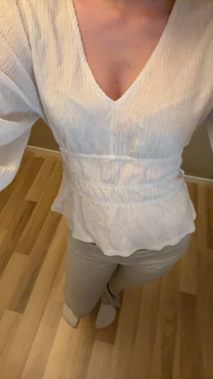 Vit blus med v-ringning och volang - Säljer en vit blus med v-ringad hals och volangkant nedtill. Blusen har långärmade puffiga ärmar 💗. Perfekt för dig som vill ha en söt blus i din garderob 💗