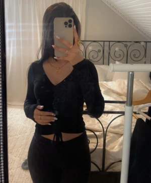 Svart croppad långärmad topp med snörning - Säljer en svart långärmad topp med v-ringning och snörning framtill som ger en snygg croppad look. Toppen har en tight passform och är tillverkad i ett mjukt, stretchigt material som sitter skönt mot kroppen. 