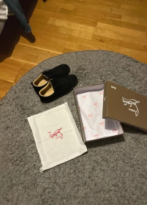 Svarta sneakers från Christian Louboutin - Säljer ett par svarta sneakers från Christian Louboutin med klassisk röd sula och snygg signatur. Skorna har rund tå, snörning och är tillverkade i mocka med diskreta detaljer. Kommer med originalkartong och dustbag. Perfekt för dig som gillar exklusiv streetstyle.