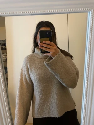 Beige fluffig polotröja med loose fit - Supermysig beige polotröja med bred krage och lång ärm. Tröjan har en loose fit och är gjord i ett fluffigt stickat material som känns extra mjukt. Perfekt för dig som gillar chill och oversized stil. Passar dig som vill ha en enkel men ändå snygg look.