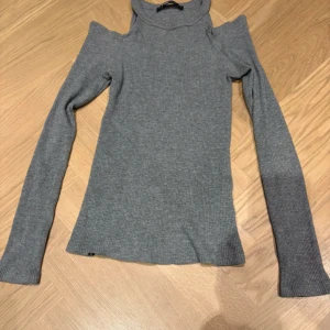Grå ribbad offshoulder tröja FB Sister - Snygg grå ribbad tröja från FB Sister i storlek S. Modellen har offshoulder-detalj och långärmade smala ärmar. Materialet är mjukt och stretchigt, perfekt för dig som gillar en slim passform och vill ha en trendig look.