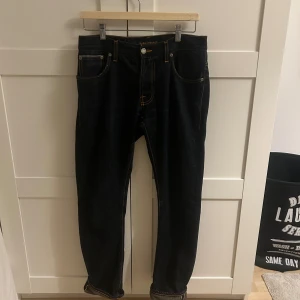 Mörkblå selvage jeans från Nudie Jeans - Mörkblå selvage jeans från nudie. I mycket bra skick använda fåtal gånger. Tvätten på jeansen ändras över tiden beroende på hur mycket du använder och tvättar jeansen. Modellen är grim Tim vilket är slim straight passform.