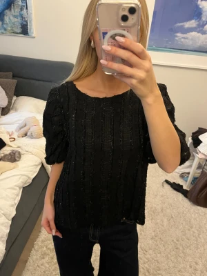 Svart glittrig blus med puffärm - Säljer en svart blus med glittriga detaljer och diskret randigt mönster. Blusen har puffiga trekvartsärmar och rund halsringning. Materialet känns lite strukturerat och ger en cool vibe. Perfekt för dig som gillar att sticka ut med stil.