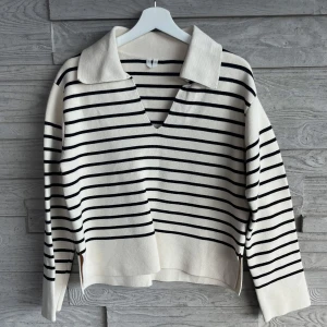 Randig stickad tröja med krage - Säljer en vit och svart stickad tröja från Arket i storlek S. Tröjan har ett randigt mönster, bred krage och v-ringad hals. Långärmad och med slits i sidorna. 