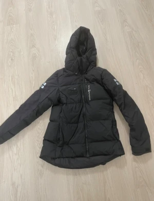 Svart Sail Racing jacka - Svart dunjacka från Sail Racing med huva jätte bra skick, använd några gånger, bra kvalite lägg gärna bud och tveka inte på att skriva till mig om du har några frågor! Ny pris: 4200kr 