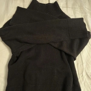 Svart stickad polotröja - Mysig svart stickad polotröja med ribbade muddar och hög krage. Tröjan har långärmade ärmar och en loose passform som gör den extra skön. Perfekt för kyliga dagar när du vill vara både bekväm och snygg.
