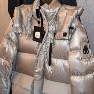 Silver pufferjacka Moose Knuckles S - Säljer en fet silverfärgad pufferjacka från Moose Knuckles, modell Adams Peak Jacket. Jackan har hög krage, stora fickor, svarta dragkedjor och logopatch på ärmen. Perfekt för kalla dagar och har en riktigt clean look. Självklart är jackan äkta. Säljs för 8000kr HELT NY köpte fel strl NYPRIS 10.000kr