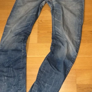 G-Star Raw ARC 3D Slim jeans blå - Säljer ett par G-Star Raw ARC 3D Slim jeans i blå tvätt med snygga slitningar och markerade veck på baksidan av benen. Jeansen har klassisk femficksdesign, smal passform och coola detaljer som kontrastsömmar. Perfekt för dig som gillar streetwear och modern stil. Lagade i mitten men det syns ej vid användning, mycket bra skick.