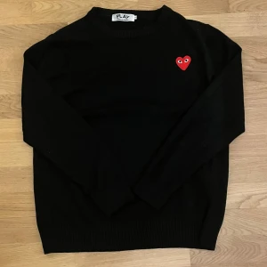 Svart tröja från Comme des Garçons - Svart stickad tröja från Comme des Garçons PLAY med ikoniskt rött hjärta på bröstet. Rund hals och långa ärmar. Storlek L men passar bättre som storlek M