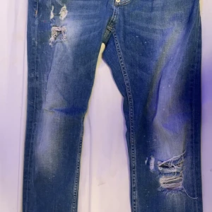Blå ripped jeans från Dsquared2 - Snygga blå jeans från Dsquared2 med slitna detaljer och trasiga partier på benen. Modellen har klassisk femficksdesign, knappgylf och coolt tvättad look. Jeansen har en rak passform och är tillverkade i robust denim för en trendig streetstil.