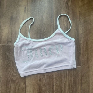 Ljusrosa Juicy Couture linne - Säljer en ljusrosa linnetopp från Juicy Couture med smala axelband och vit kant. Toppen har glittrande stenar som bildar texten 'Juicy' på framsidan. Materialet är mjuk polyester med lite stretch för skön passform. Perfekt för dig som gillar Y2K-vibe!