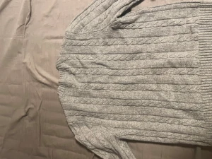 Grå kabelstickad tröja Polo Ralph Lauren - Snygg grå kabelstickad tröja från Polo Ralph Lauren i storlek S. Tröjan har rund hals, ribbade muddar och ett diskret broderat logomärke på bröstet. Perfekt för dig som gillar klassisk stil med en modern touch.