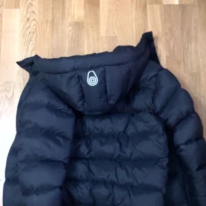 Svart dunjacka från Sail Racing - Köp Gärna en Svart dunjacka från Sail Racing med luva och diskret logga på bröstet. Jackan har puffad design, dragkedja framtill och är riktigt skön för kalla dagar. Perfekt för dig som vill ha en stilren och varm jacka med sportig vibe. Den är Också helt Ny. Nypris 2500. Mig= 1500