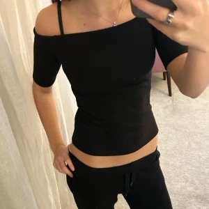 Svart ribbad offshoulder topp - Säljer en svart ribbad topp med offshoulder-design och korta ärmar. Toppen har en tight passform och är tillverkad i ett stretchigt material som sitter snyggt mot kroppen. Perfekt för dig som gillar stilrena och enkla plagg med en modern touch.