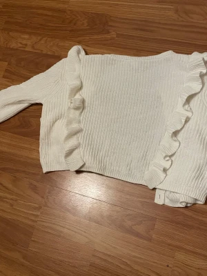 Vit kofta med volanger från Lindex - Superfin vit stickad kofta från Lindex med volangdetaljer längs framstycket och knappar hela vägen. Koftan har långärmade ribbstickade ärmar och rund hals. Perfekt för dig som gillar en söt och trendig look.