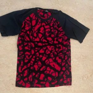 Jordan t-shirt med röd camouflage - Säljer en cool t-shirt från Jordan i storlek M. Framsidan har ett rött och svart camouflage-mönster med den klassiska Jumpman-loggan broderad på bröstet. Ärmarna är svarta och korta, och materialet känns som mjuk bomull. Perfekt för dig som gillar streetwear. Funkar även till andra typer av klädstilar, t-shirten är knappast använd och fungerar felfritt. ABS! Pris går att diskutera! 