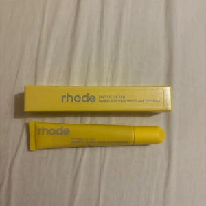 Rhode Peptide Lip Tint  - Rhode Peptide Lip Tint i en snygg gul tub med matchande förpackning. Läppbalsamet har en mjuk formula som ger läpparna en hint av färg och extra fukt. Perfekt att ha med i väskan för att boosta läpparna med glow och näring.