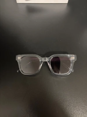 Transparenta solglasögon CHIMI Grey - Snygga solglasögon från CHIMI med transparent fyrkantig båge och gråtonade linser. Modellen heter Grey 04 och har en modern, stilren look som passar dig som gillar cleana accessoarer. Bågen är i syntetmaterial och detaljerna är diskreta men coola.