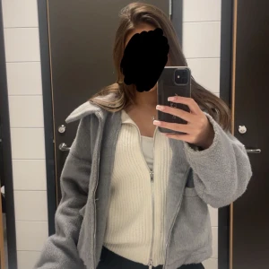 Grå jacka med dragkedja - Säljer en supermjuk och fluffig grå jacka med stor krage och dragkedja framtill. Jackan har en loose passform och är perfekt för dig som gillar chill och cozy vibes. Fickor på sidorna och framförallt skön!