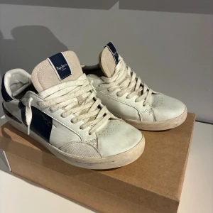 Pepe Jeans - Sneakers (stl 42) - Säljer ett par vita och marinblå sneakers från Pepe Jeans i storlek 42. Skorna är i bra skick, utan några defekter. De är använda men inte överdrivet mycket, och har endast vanligt lätt slitage. Modellen har varit väldigt populär och är känd för att vara både skön och stilren. Passar bra till både vardagskläder och mer uppklädda outfits. Levereras med originalkartong.  Nypris ca 799–999 kr.
