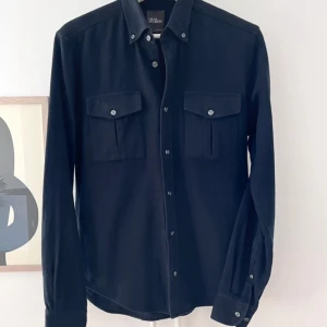 Marinblå skjorta Oscar Jacobson slim S - Svart skjorta från Oscar Jacobson i slim fit med klassisk krage och två bröstfickor med knappar. Tillverkad i 100% bomull, långärmad och med knappar längs hela framsidan. Perfekt för dig som gillar stilrena och enkla plagg. Jättesnygg hade haft kvar ifall den passa men för liten passar xs/S. Köpt på nk helt ny 
