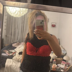 Röd spets korsett med rosett - Säljer en snygg röd korsett med spetsdetaljer och liten rosett framtill. Toppen är tight och har axelband, perfekt att styla över en svart ärmlös topp eller för sig själv. Ger en cool och edgy vibe till din outfit.