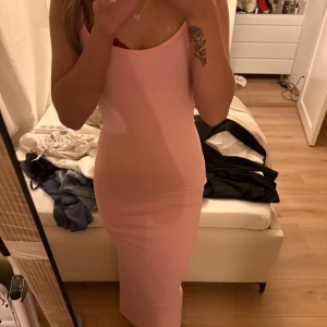 Ljusrosa långklänning med smala axelband - Säljer en superfin ljusrosa långklänning med smala axelband. Klänningen har en tight passform och är ärmlös, perfekt för dig som gillar en enkel men snygg look. Materialet känns mjukt och stretchigt, vilket gör den bekväm att bära hela dagen.