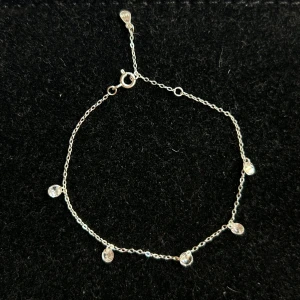 925 silverarmband med kristaller Glitter - Ett stilrent och nätt armband i äkta silver med fem små runda kristaller som hänger längs den tunna kedjan. Perfekt för dig som gillar minimalistiska smycken med lite extra bling. Lås med klassisk ring och justerbar längd. (16-17cm) Från glitter nypris 299kr