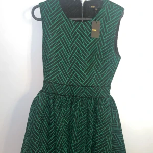 Grön och svart mönstrad klänning Maje - Supersnygg grön och svart kort klänning från Maje med coolt grafiskt mönster. Ärmlös modell med markerad midja och dragkedja bak. Priset kan diskuteras. Storlek 38 dam.