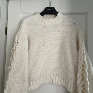 Stickad tröja - Stickad tröja med lös passform. Tröjan har rund hals ringning med ribbad stickad kant, nedhasad axel och lång ärm med kabelstickad parti och snörning. Ribbstickad kant vid ärmslut och ned till💕pris kan diskuteras 