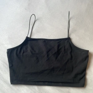 Svart linnetopp från NA-KD - En svart, enkel linnetopp från NA-KD med tunna axelband och rak skärning. Perfekt att styla med jeans eller kjol för en clean look. Tillverkad i mjuk bomull som känns skön mot huden.