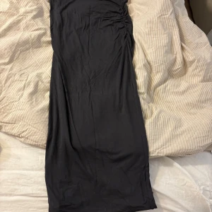 Grå långkjol från Gina Tricot - Grå långkjol från Gina Tricot i mjukt och stretchigt material. Kjolen har en bred resår i midjan och snygga rynkade detaljer längs sidan som ger en cool look. Passformen är normal och tyget känns lätt mot huden.