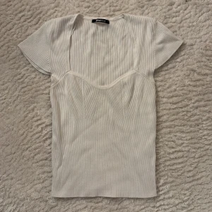 Vit ribbad topp från Gina Tricot - Storlek M men passar även mig som brukar ha s Supersnygg vit ribbad topp från Gina Tricot med markerad byst och korta ärmar. Toppen har en figurnära passform och coola sömdetaljer framtill som ger en modern look. Perfekt att styla med jeans eller kjol för en trendig outfit.