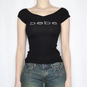 Svart topp med strasslogga från Bebe - Svart tight topp från Bebe med korta ärmar och snygg v-ringning. Framsidan har Bebe-loggan i glittrande strass. Första bilden är från Pinterest men den är väldigt lik!! 🩷🌸fint skick förutom några rhinestones som fallit av (se bild)