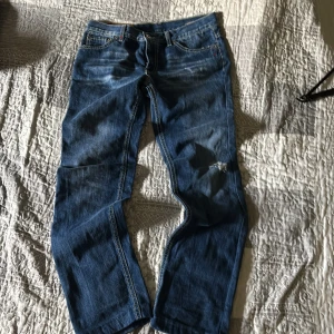Blå jeans från Dondup med slitning - Säljer ett par blå jeans från Dondup med snygga slitningar och en liten reva på ena benet. Klassisk femficksmodell med orange sömmar och skön passform. Jeansen har en cool tvättad look och är tillverkade i bomull. Perfekta för dig som gillar en avslappnad stil. De är mer åt skinny håller och de är för 12-14 år skulle jag säga 