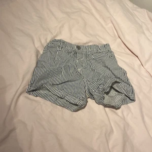 Randiga blåvita shorts i bomull - Säljer ett par snygga blåvita shorts med smala ränder. De har klassisk passform med knapp och dragkedja framtill samt fickor på sidorna. Perfekta för varma dagar och riktigt sköna tack vare det tunna bomullsmaterialet.