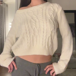 Vit stickad tröja  - Supermysig vit stickad tröja med kabelstickat mönster och croppad passform. Tröjan har offshoulder-stil och långa ärmar med breda muddar. Perfekt för lager-på-lager och chill dagar.