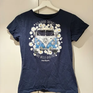 Söt t-shirt - Mörkblå t-shirt med tryck av en blå hippiebuss omgiven av vita prästkragar och texten 'All good things are wild and free'. Rund halsringning och korta ärmar. Perfekt för dig som gillar retrostil och coola prints. Vill bli av med den, priset är diskuterbart!! Knappt använd!