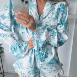 Set med blus och shorts med fint mönster i vitt och blått/ljusblått - Set med blus och shorts med fint mönster i vitt och blått/ljusblått, one size, passar S-L. Resår i midjan på shortsen och rymlig topp. Mycket fint mönster, klassisk stil. Aldrig använt.