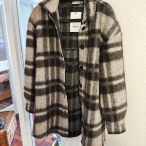 Rutig jacka från Gestuz, stl 36 - Snygg och trendig jacka från Gestuz i storlek 36. Jackan har ett rutigt mönster i beige och mörkbrunt, stora knappar framtill och mjukt ullblandmaterial. Perfekt för lager-på-lager och ger en cool vibe till din outfit.