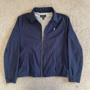 Marinblå vindjacka från Ralph Lauren - Klassisk marinblå vindjacka från Ralph Lauren. Den har inga skador och passar perfekt nu som en tunnare jack till hösten. Den är i riktgt bra skick och har inga skador. 😊🤩