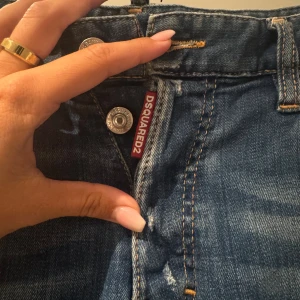 Dsquared2 Cool Guy jeans blå, stl 48 - Säljer ett par Dsquared2 Cool Guy jeans i blå tvätt med slitningar, hål och färgstänk för en edgy look. Klassisk femficksmodell med knappgylf och Dsquared2-logga vid midjan. 